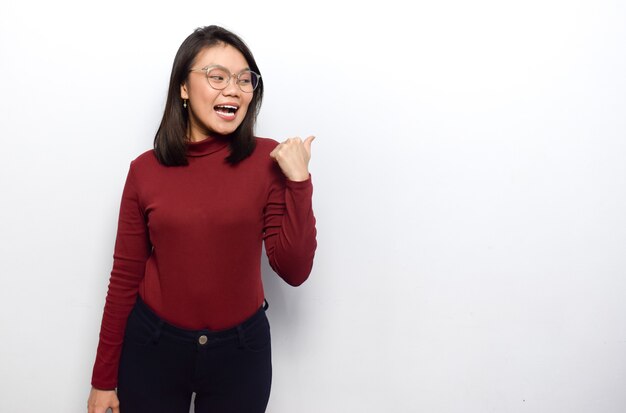 Pointing to the right with thumb of Young beautiful asian women dress red shirt isolated on white