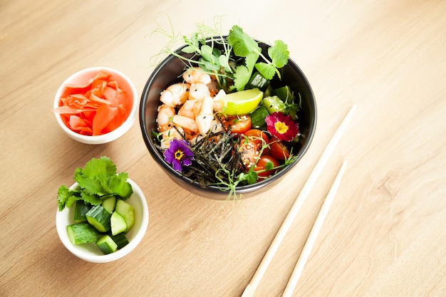 Poke salad with shrimp in a bowl. Ingredients Shrimp, blanched spinach, cherry tomatoes, rice, cucumber, soy-ginger sauce, Spicy sauce, nori, sesame, lime, cilantro. Asian seafood salad concept.