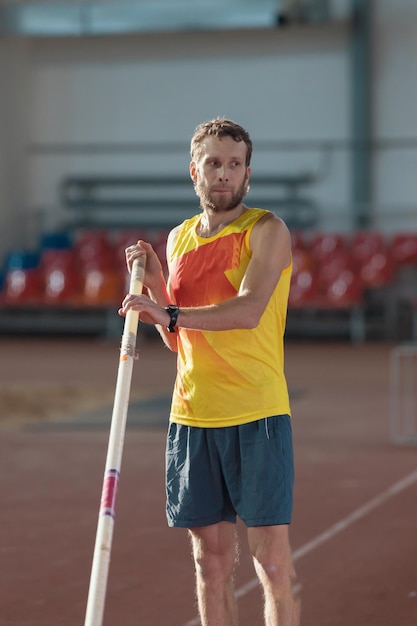 Pole vaulting indoors a man in yellow shirt standing on the track with a pole sports stadium