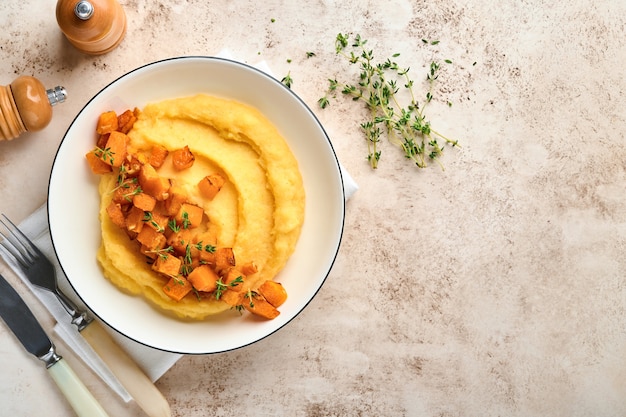 polenta with butter, pumpkin, garlic, savory and parmesan cheese in white bowl on light concrete