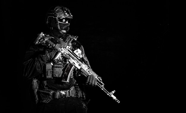 Police assault team member, special forces soldier, private security service, military company serviceman in black ammunition and uniform, armed service rifle, high contrast studio shoot on black