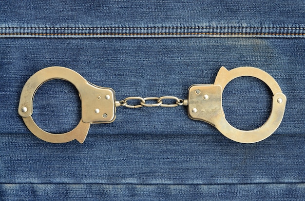 Police steel handcuffs lying on dark blue jeans background 