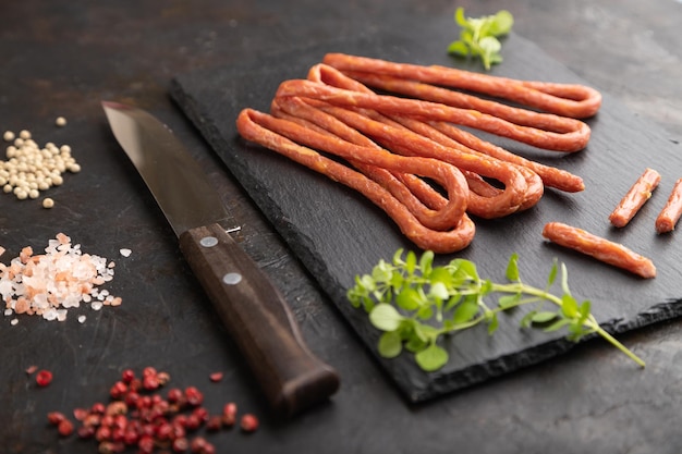 Polish smoked sausage kabanos on a slate cutting board on black concrete background Side view close up selective focus