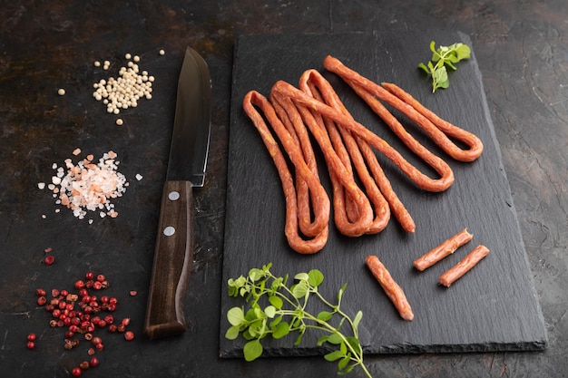 Polish smoked sausage kabanos on a slate cutting board on black concrete background Side view close up