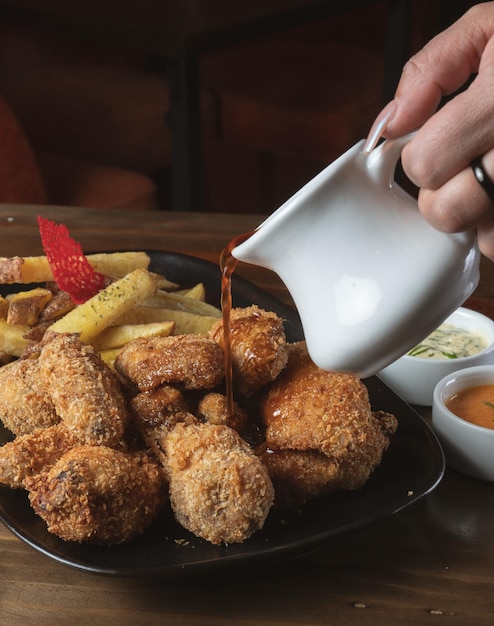 Pollo frito con papas fritas y cremas con un fondo de madera.