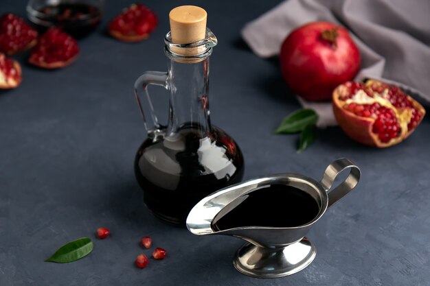 Pomegranate sauce in a bottle and gravy boat with grains and pieces of pomegranate on dark