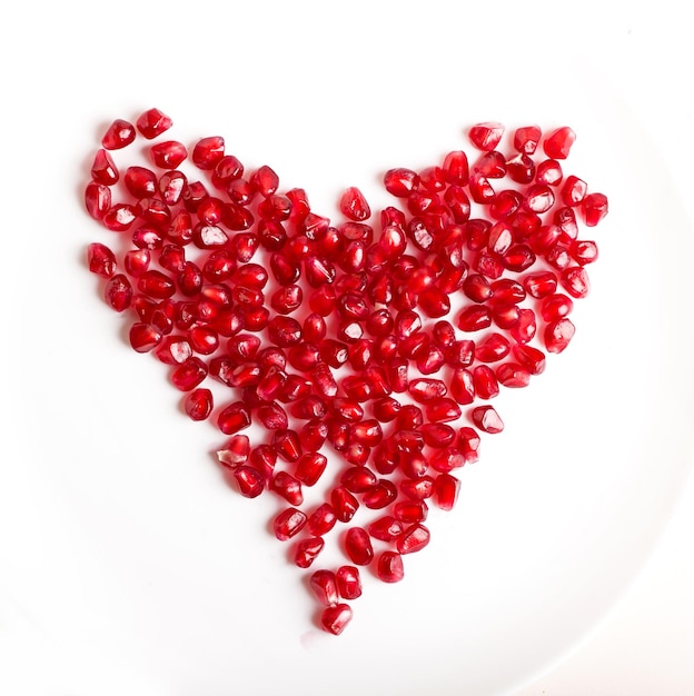 Pomegranate seeds in the form of a heart on a white background Cut the pomegranate with scattered grain top view isolated on white background