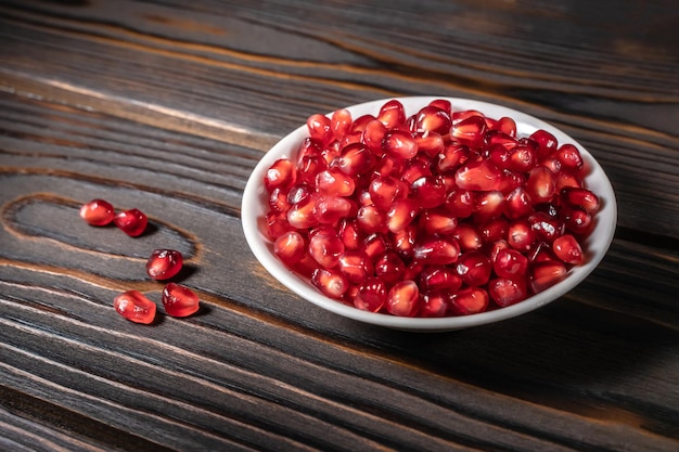 Pomegranate seeds heap in white plate on dark wooden background