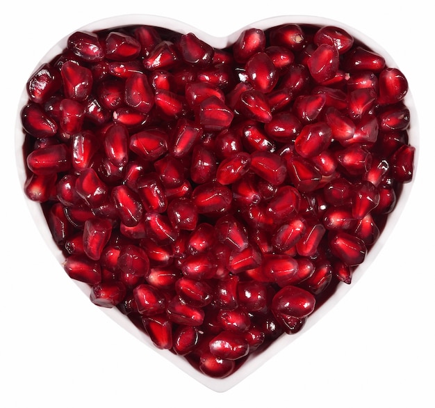 Pomegranate seeds in plate in the form of heart on a white background