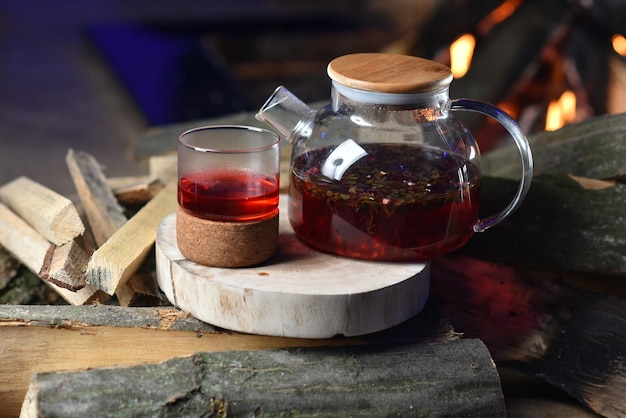 Pomegranate tea in a glass transparent teapot against the background of firewood and a fire