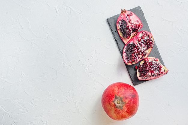 Pomegranates whole and cut over white textured background, top view with space for text.