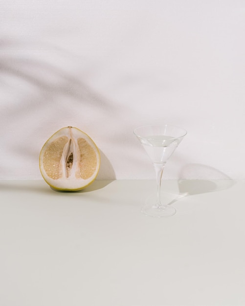 Pomelo and cristal glass with liquid on pastel green and white background Soft palm leaves shadows