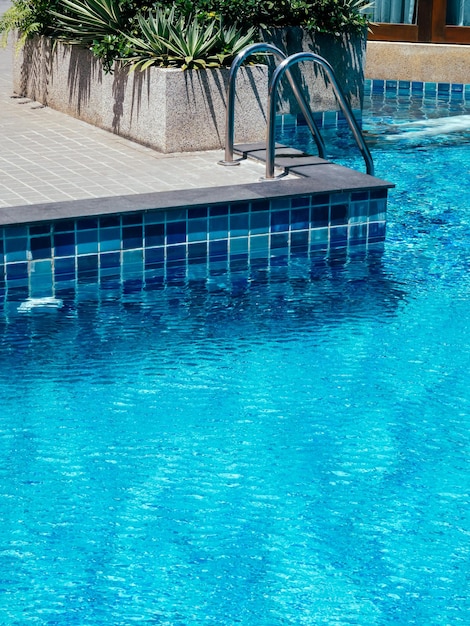 Poolside decoration with green leaves in the stone block near the ladder at the swimming pool with copy space vertical style Empty outdoor pool on sunshine day in summer