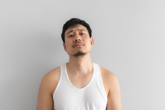 Poor and depressed man wear white tank top on grey background.