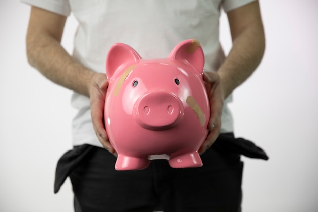 Poor man with empty pockets holding large broken piggy pank with bandages on it