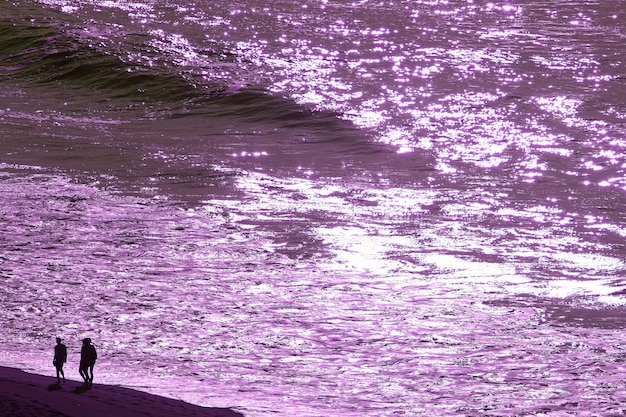 Pop art surreal style purple colored wavy sea with the silhouette of people walking along the beach