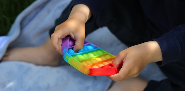 Pop it silicone anti-stress toy. The child plays on the grass. New trend Selective focus. Nature