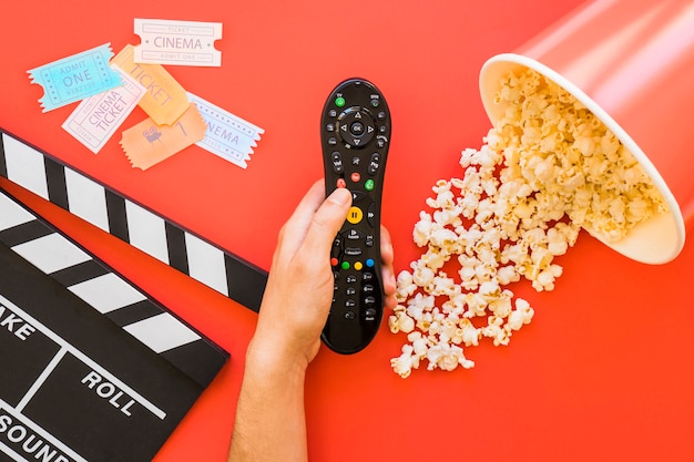 Popcorn, clapperboard and hand holding remote control