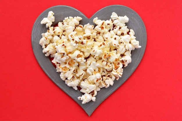 Popcorn in heart frame on red background closeup