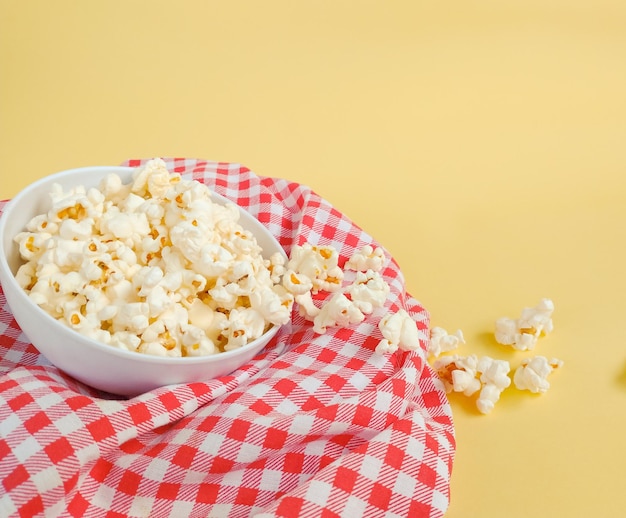 Popcorn inside bowl on top of checkered cloth on yellow background