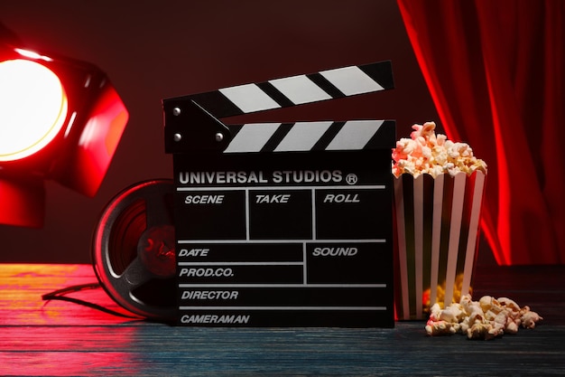 Popcorn in paper cup clapperboard reel and spotlight on dark background