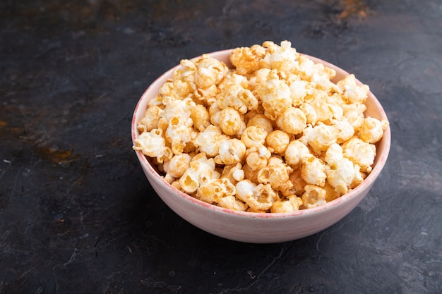 Popcorn with caramel in ceramic bowl on a black concrete surface