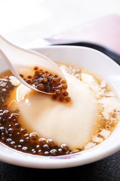 Popular Taiwan gourmet Dessert of tapioca pearl ball bubble mixed bean curd tofu pudding douhua dou hua in white bowl close up lifestyle