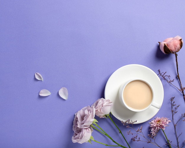 Photo porcelain cup with coffee and beautiful lilac roses, dried flower branches on a lilac background. spring coffee concept. flat lay style, top view, place for text