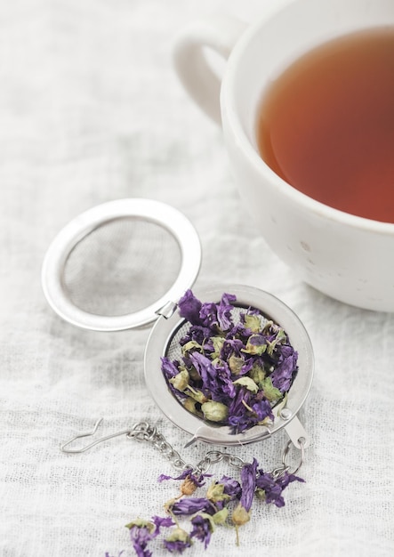 Porcelain cup with hot tea and infuser with loose blue mallow tea on white towel