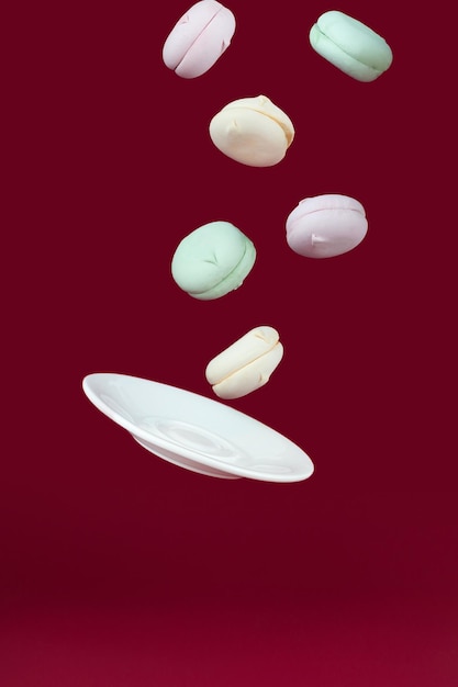 Porcelain saucer flying with marshmallows on a red background concept of sweet dessert Gravity