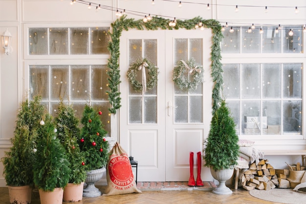 Porch with a white door in Christmas decorations and Christmas trees.