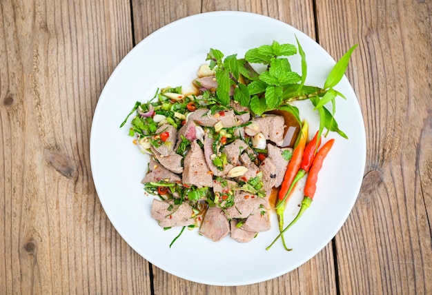 Pork liver salad with fresh chili herbs spices Spicy liver salad on white plate wooden table background Thai food