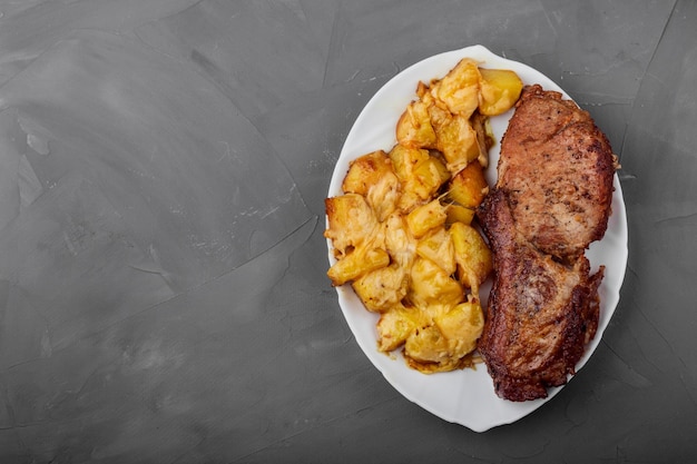 Pork loin steak and potatoes baked with cheese on a white plate gray background