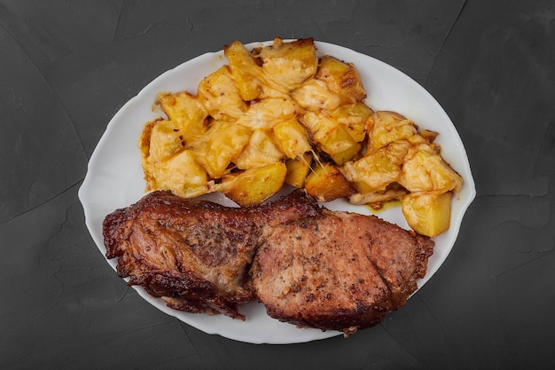 Photo pork loin steak and potatoes baked with cheese on a white plate