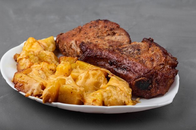 Pork loin steak and potatoes baked with cheese on a white plate