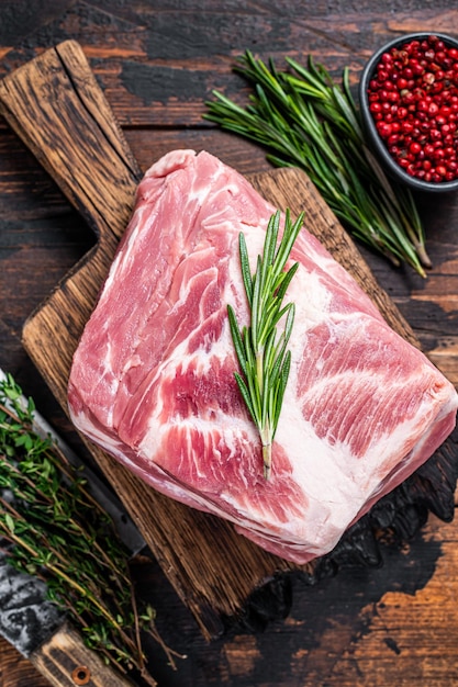 Pork neck raw meat for fresh Chop steaks on wooden cutting board with butcher cleaver. Dark wooden background. Top view.