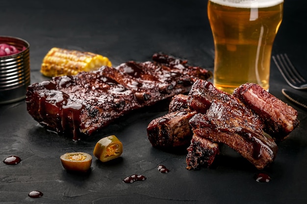 Pork ribs in barbecue sauce and a glass of beer on a black slate dish A great snack to beer on a dark stone background Top view with copy space