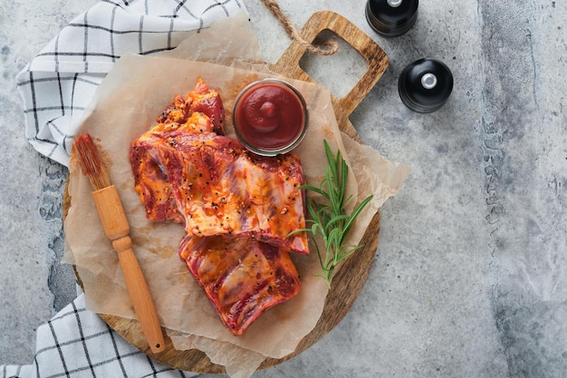 Pork ribs Raw meat Raw pork ribs in marinade with spices rosemary tomato sauce and garlic on old wooden stand on black stone table background Barbecue concept Top view Mock up