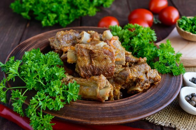 Pork ribs steamed with carrots, parsley decorated in a clay bowl on a wooden background. Close up