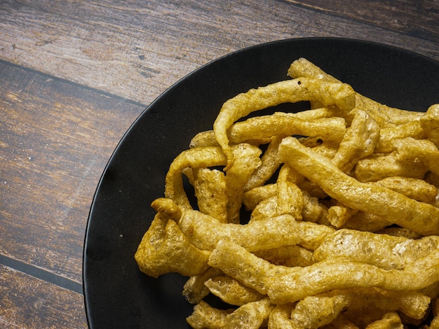 Pork rind in black plate on wood table for food concept