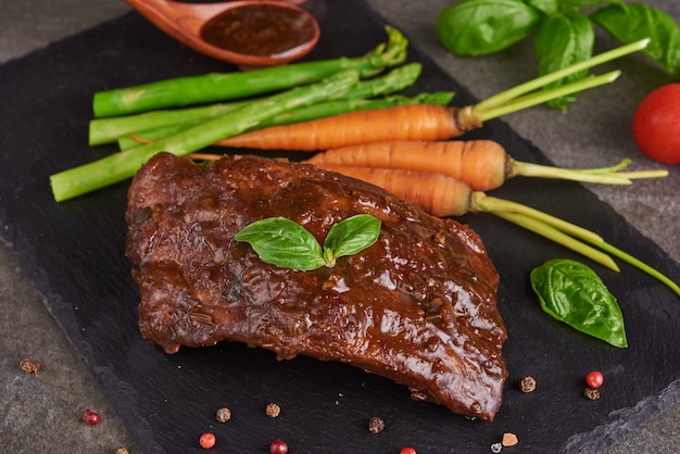 Pork roasted, grilled spare ribs from a summer BBQ served with Vegetables, asparagus, baby carrots, fresh tomatoes and  spices. smoked ribs on Black stone surface. top view,