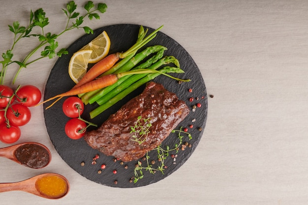 Pork roasted, grilled spare ribs from a summer BBQ served with Vegetables, asparagus, baby carrots, fresh tomatoes and  spices. smoked ribs on Black stone surface. top view,