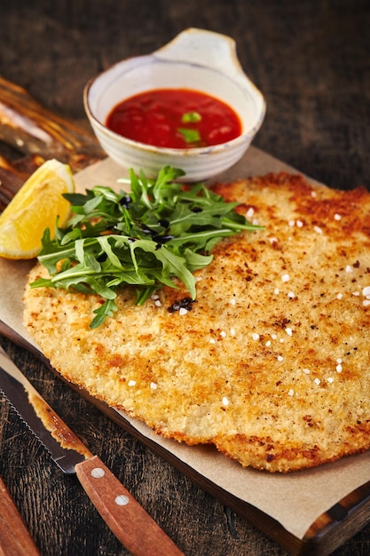 Pork schnitzel with tomato sauce on dark wooden background