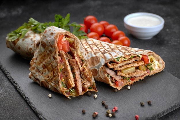 Pork shawarma, on a black background, with herbs, tomatoes and sauce