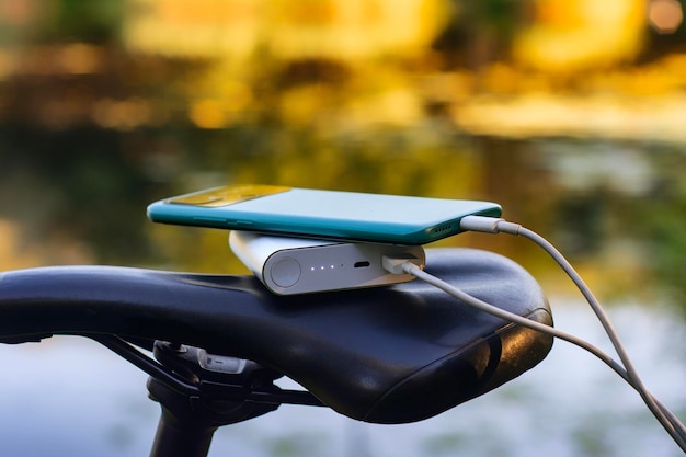 A portable charger charges a smartphone on the background of a bicycle and nature Power Bank on a journey to charge gadgets