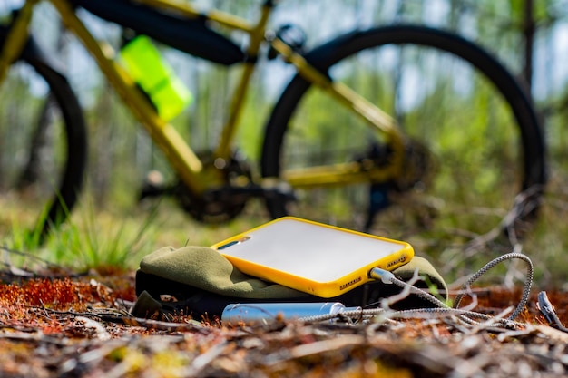 A portable charger charges the smartphone Power Bank with cable against the background on the forest and bicycle