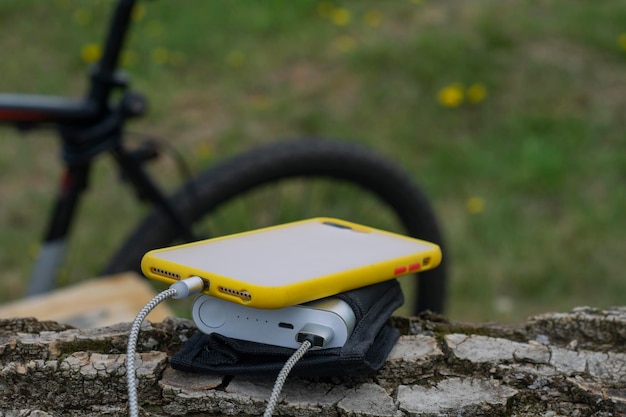 A portable charger charges the smartphone Power Bank with cable against the background of wood and bicycle