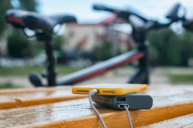 A portable charger charges the smartphone Power Bank with cable against the background of wooden bench and bicycle