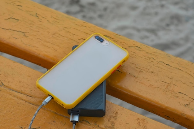 A portable charger charges the smartphone Power Bank with cable against the background of wooden bench