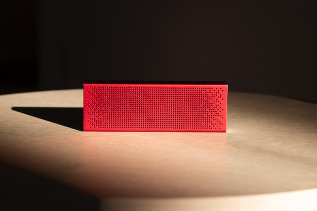 Portable red music speaker located on a wooden table in the sun